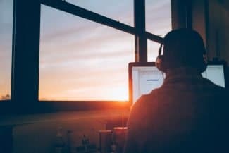 Man attending a webinar while the sun sets.
